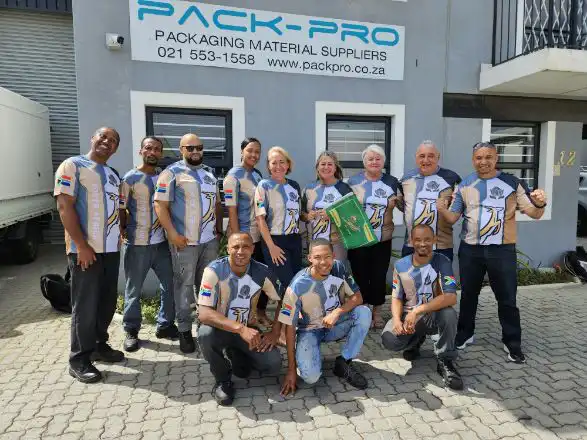 Pack-Pro-Team Group of twelve employees in matching blue-gray jerseys posing outside the Pack-Pro Packaging Material Suppliers building.